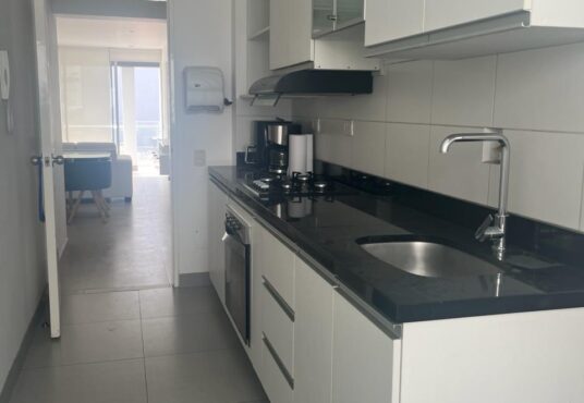 En venta departamento en Miraflores con cocina en galería con desayunador. Excelente distribución con muebles altos y bajos. Iluminación y ventilación óptimas. Se aprecia la sala/comedor al fondo con luz natural desde el balcón Ubicado en exclusiva calle Roma.